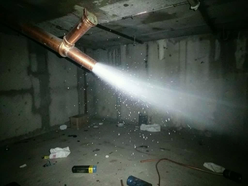 A burst pipe spraying water through a flashlight beam in a dark utility room